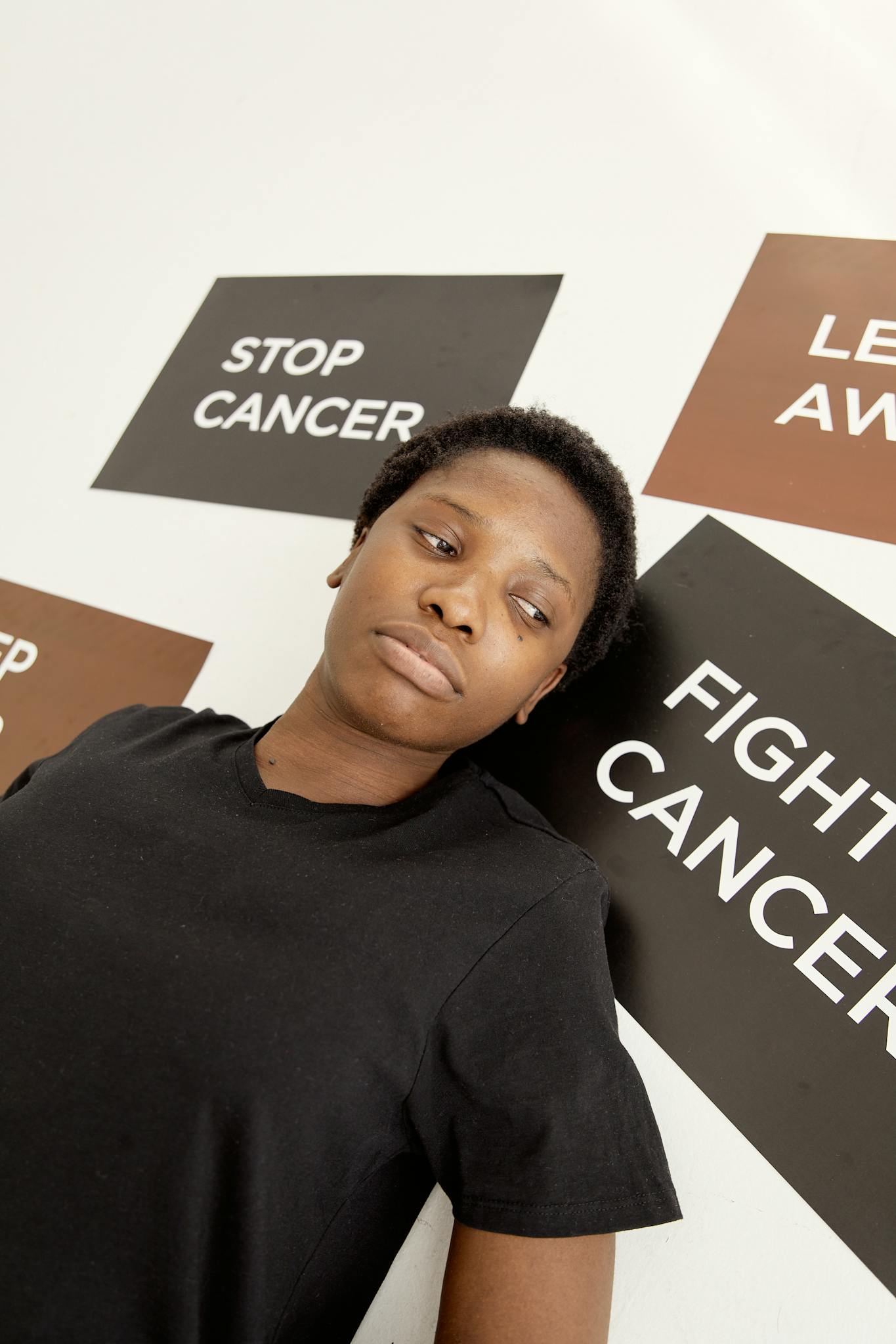 Black woman standing against a wall with cancer advocacy placards, promoting awareness and strength.