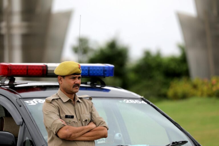 Indian police officer with arms crossed standing by a patrol car outdoors, showcasing authority and law enforcement presence.